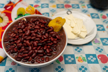 Cooked red beans and yellow plantain in a bowl with raw cheese and sour cream in a plate at the side. Traditional food from Central America, South America and Latin America. 