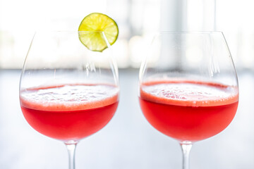 Macro closeup of two glasses goblets of red watermelon and lime juice agua fresca tropical beverage with slice of fruit and bokeh background in summer