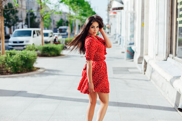 Fototapeta premium beautiful woman in a summer red dress walks down the street