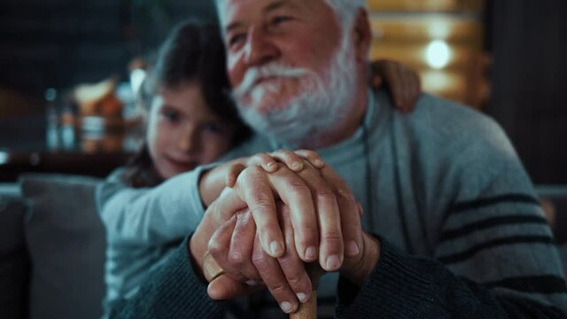 Portrait of a hugging family holding hands on grandpa's walking stick. Compassionate child girl supporting old retired grandfather