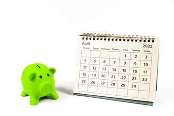 April 2022 calendar and green piggy bank on white background