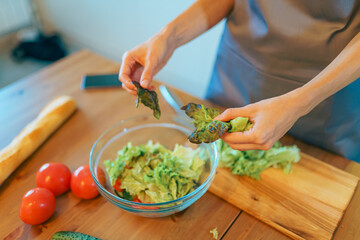 Young woman cutting fresh vegetable salad in modern cozy kitchen interior, prepare healthy meal