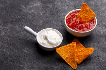 Sour cream and red chili sauce served with corn nachos, over black background. Mexican snack