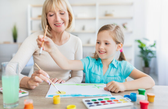 Granny and granddaughter drawing with watercolor paints at home