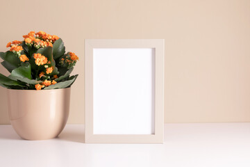 Blank photo frame mockup and kalanchoe plant with orange flowers in pot on beige background.