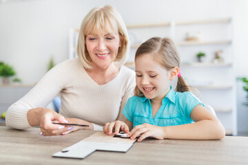 Happy mature woman and granddaughter solving jigsaw puzzle