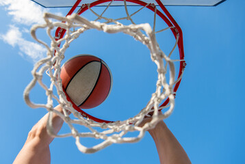 guy dunking basketball ball through net ring with hands, targeting © Olena