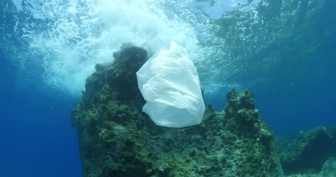 plastic bag underwater bad for fish with sun rays water waves hit to rocks background ocean pollution