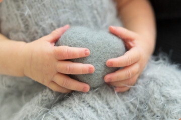 Newborn's hands hold the gray toy heart