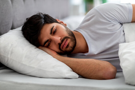 Sad arab guy lying alone in bed, suffering from loneliness and thinking of problems. Male stress and depression concept