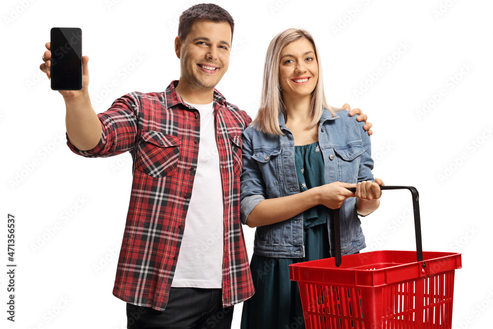 Wall mural young couple with a shopping basket showing a smartphone and smiling at camera