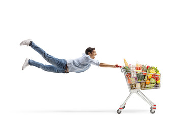 Full length shot of a casual young man flying with a shopping cart with food