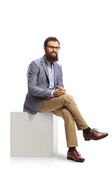 Bearded man sitting on a white cube and smiling