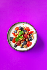 Yogurt with forest berries in bowl on orange background