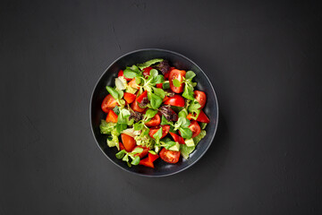 Tomatoes and cucumbers vitamin salad in a black plate, black background. Healthy food concept.