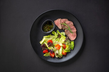 Spicy Beef Slices Meat Salad with Tomatoes, Cucumber and Salad leaves on black table