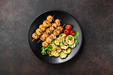 Grilled shrimp skewers. Seafood, shellfish. Shrimps Prawns skewers with spices and fresh herbs and vegetables on black stone background, copy space. 