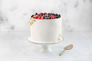 Beautiful tasty white cake with white cream and berries; on cake stand
