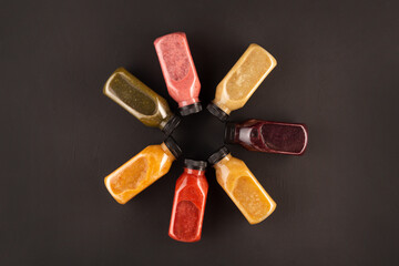 Flat-lay of colorful smoothies in bottles with fresh tropical fruit and superfoods on concrete background