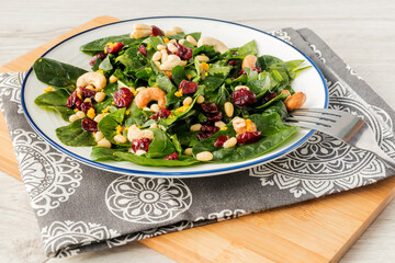 On a white platter, a delicious fresh healthy salad of spinach leaves, pine nuts, dried...