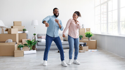 Satisfied young african american husband and wife dancing in new apartment with cardboard boxes