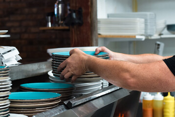 Restaurant kitchen employee placing stack of clean dishes on a shelf