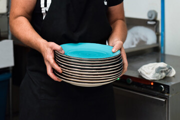 Restaurant kitchen employee carrying stack of clean dishes