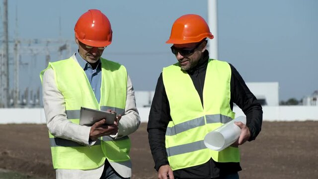 Wind alternative power generated by windmill. Engineers in orange helmets discuss walking from transformer substation in countryside