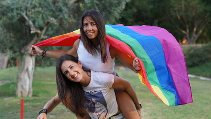 Chicas jóvenes lesbianas con bandera LGTBI jugando llevándose a coscoletas o al caballito