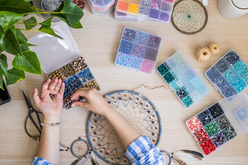 Artistic female hands use colorful beads for creating native tribal Indian amulet dreamcatcher