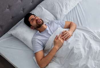 Thoughts in head not let fall asleep. Young arab man lying in bed and looking at ceiling, thinking...