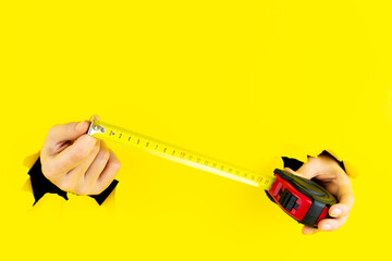 .Female hands is holding measuring tool, construction tape measure roulette in torn holes of yellow...
