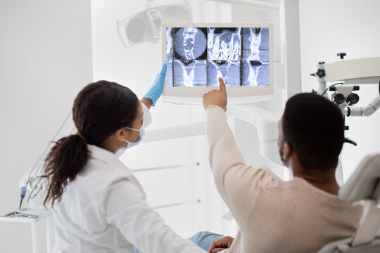 Black Female Stomatologist Showing Teeth Xray Picture On Digital Monitor To Patient
