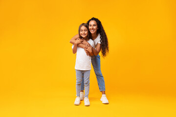 Middle-Eastern Mother Hugging Her Lovely Little Daughter On Yellow Background