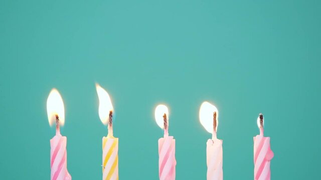 Happy Birthday concept Made of Burning Colorful Candles on blue or turquoise background. Blowing out five years anniversary birthday candles. Two candles do not want to go out.