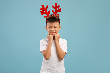 Making Wish. Little asian boy wearing xmas reindeer horns dreaming about something