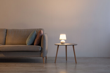 Couch with pillows, glowing lamp on table at home on gray wall background