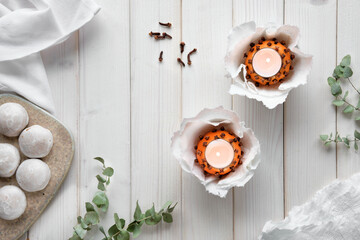 Fototapeta na wymiar Wintertime background, desktop with eucalyptus twigs, candles in natural pomander ball orange and gingerbread cookies with white icing. Flat lay, top view on off white rustic wooden table.