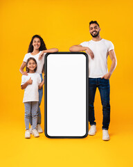 Middle-Eastern Family Standing Near Big Blank Phone Screen, Yellow Background