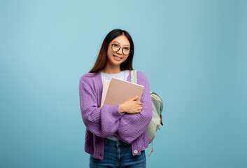Academic education. Asian lady with backpack and notebooks smiling at camera on blue studio background