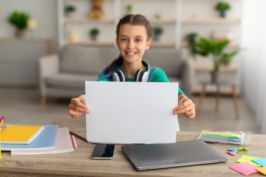 Girl sitting at desk, showing sheet of paper