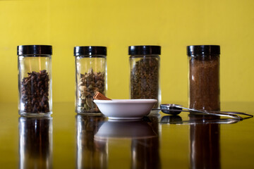 Glass jars of Indian spices in the backdrop with cinnamon in a white bowl and measuring spoons on a...