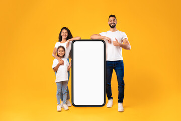 Arabic Family Standing Near Big Blank Smartphone Screen, Yellow Background