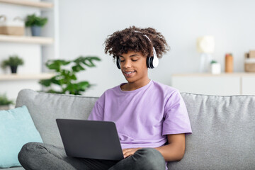 Remote education. Cool black teen guy in headphones having online lesson, participating in webinar...