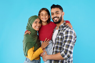 Muslim Parents Embracing Little Daughter Posing Together Over Blue Background