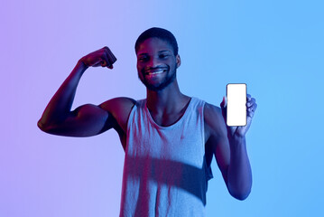 Cheerful black guy showing cellphone with blank screen, demonstrating muscles in neon light, mockup...