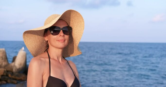 Woman enjoy light breeze. A good looking woman in sunglasses and hat relax on the sea beach under the sun.