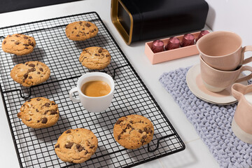 Seven chocolate chip cookies over a black metallic cooling rack around a white cup of coffee.