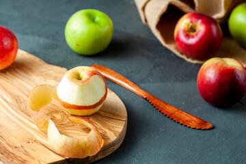 apples of different varieties are seen on dark stone and wooden background. still life image with half peeled apple and wooden knife. Versatile concept image