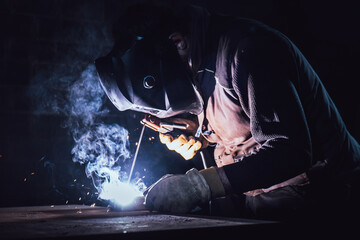 Welder welding on a table in a factory with smoke
